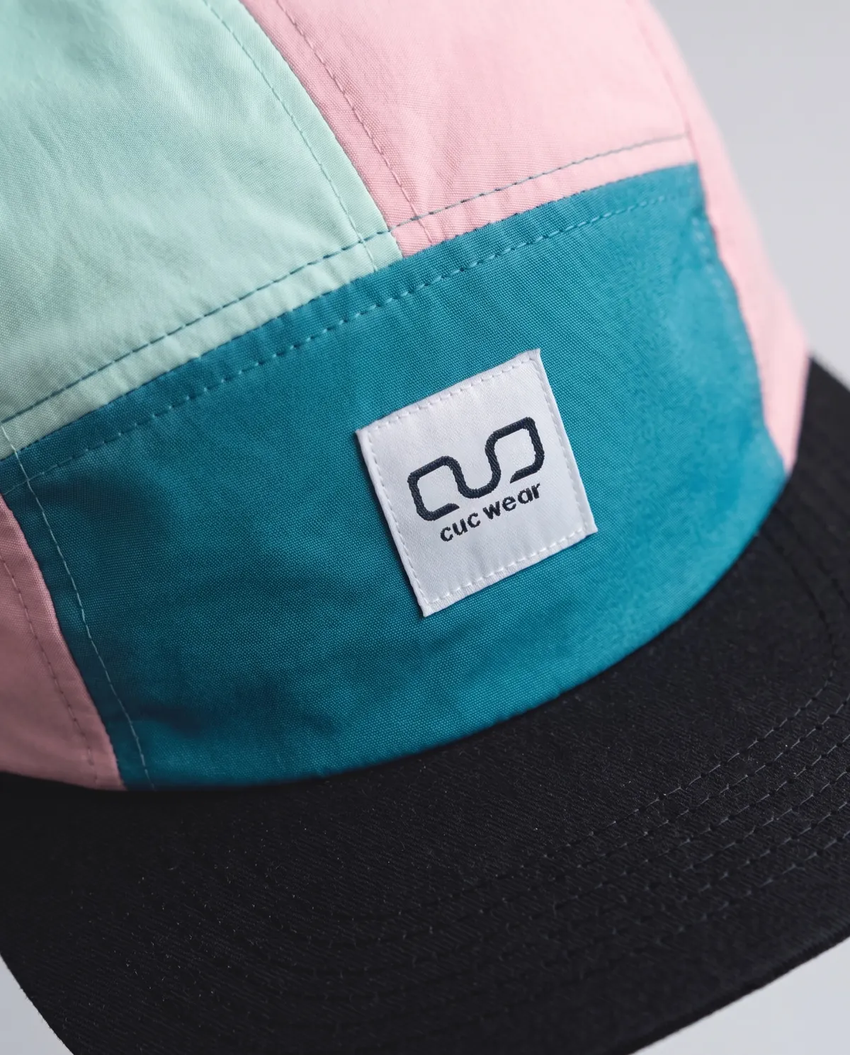 Detalle de la etiqueta cuc wear sobre una gorra de cinco paneles en tonos pastel