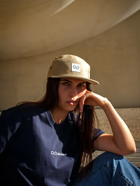 Chica con gorra khaki y camiseta Navy Essential apoyada en una pared curva de hormigón cálido