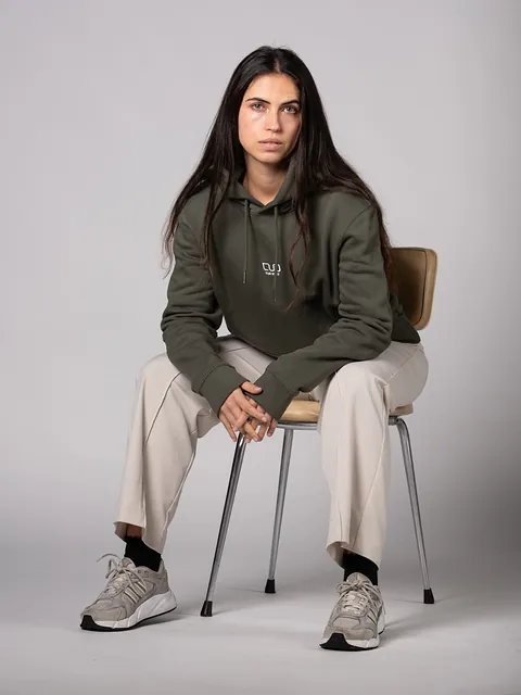 Chica con el hoodie Organic Khaki sentada en una silla de madera sobre fondo gris