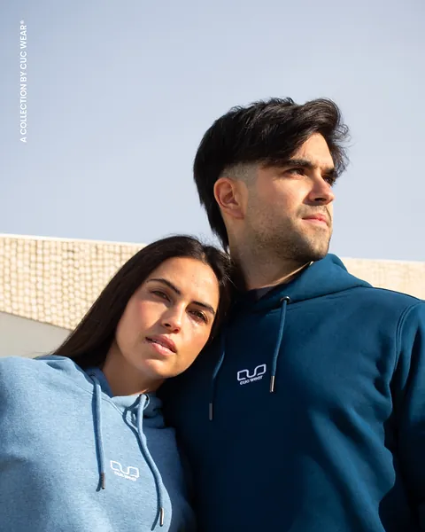 Pareja con los hoodies Cool Blue y Peacock Blue a pleno sol, mirando hacia un lado